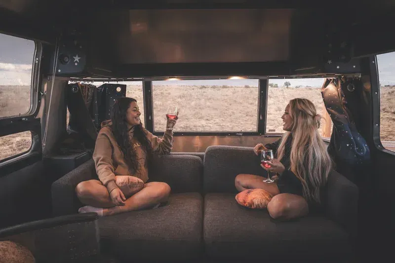 two women are sitting on a couch in a van drinking wine .