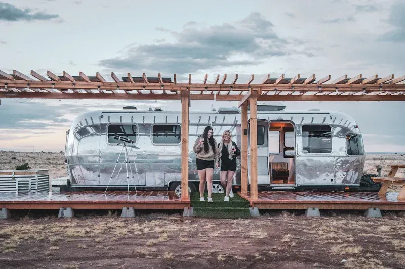 two women are standing in front of an airstream trailer .