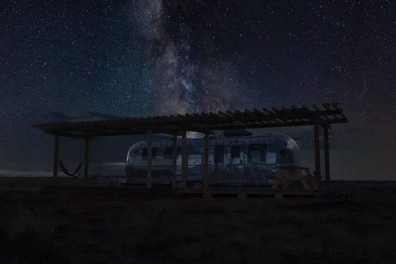 an airstream is parked under a pergola at night under a starry sky .