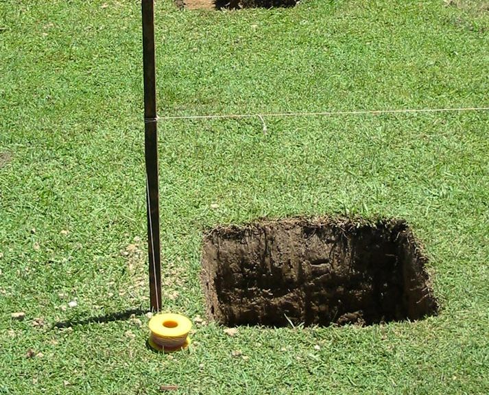 A Hole in the Grass With a Yellow Tape on It — Small Batch Concrete Delivery in Carrara, QLD