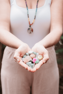 a female sound healer stands holding a handful of green, pink, and light orange crystals in her hands