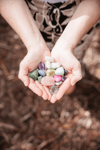 two hands holding an assortment of healing crystals in various shades of purple, blue, and pink