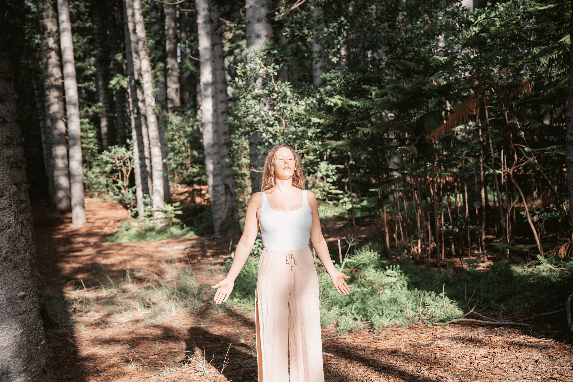 a woman standing in a forest with her arms and hands outstretched to the sun