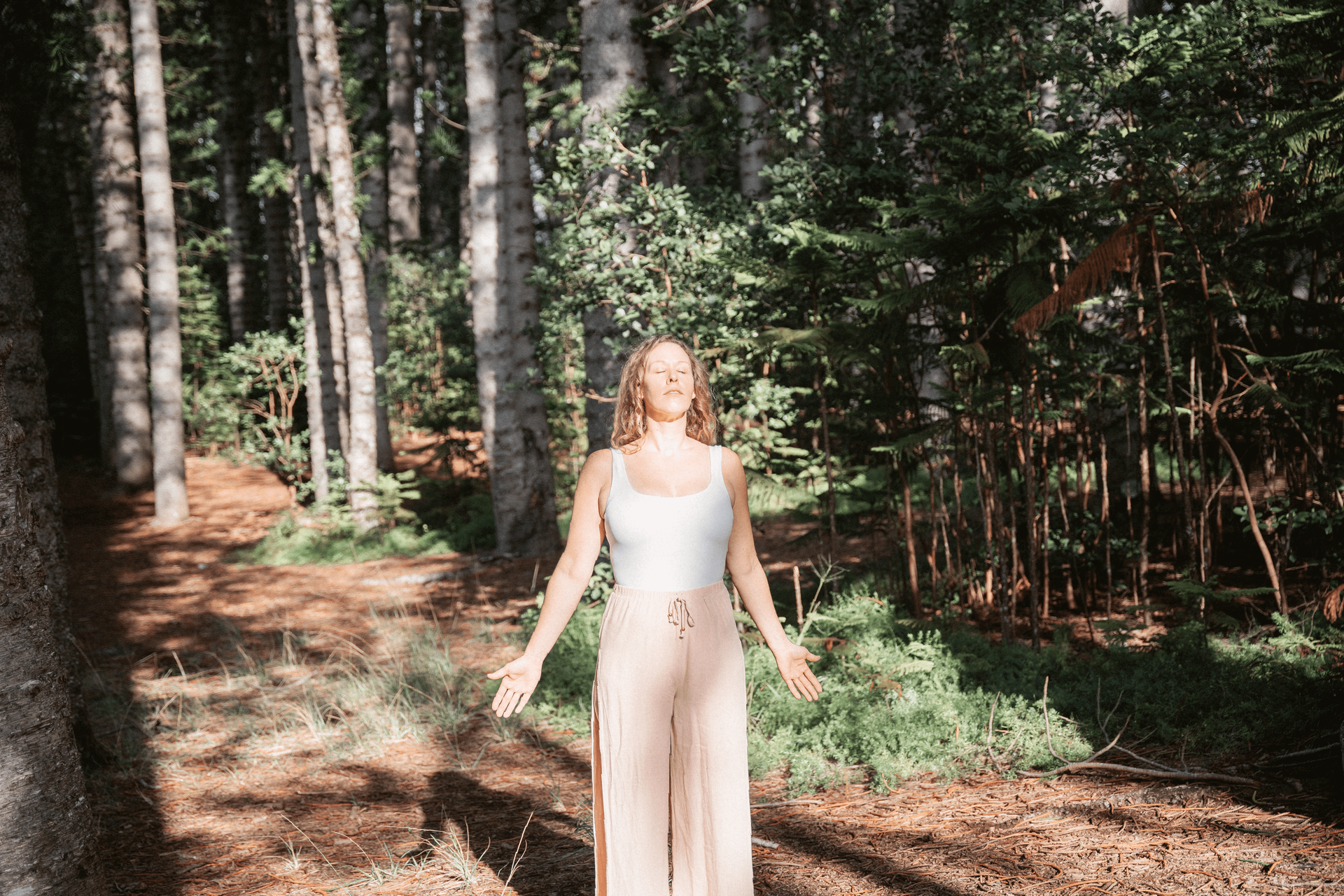 jessica minnoch, sound healer and reiki master, stands in a forest with arms and hands outstretched facing the sun