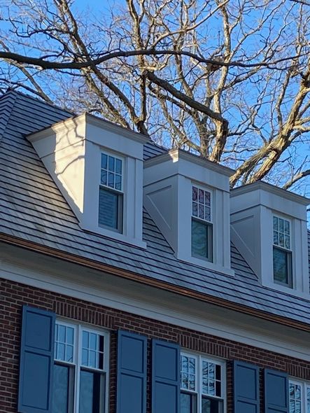 Brick home exterior with dormers, blue shutters, and a tree against a blue sky.