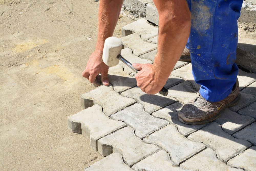 A man is using a rubber mallet to hammer bricks on a sidewalk.