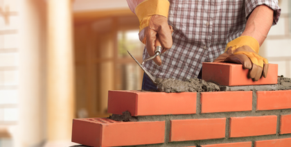 A man is building a brick wall with bricks and cement.