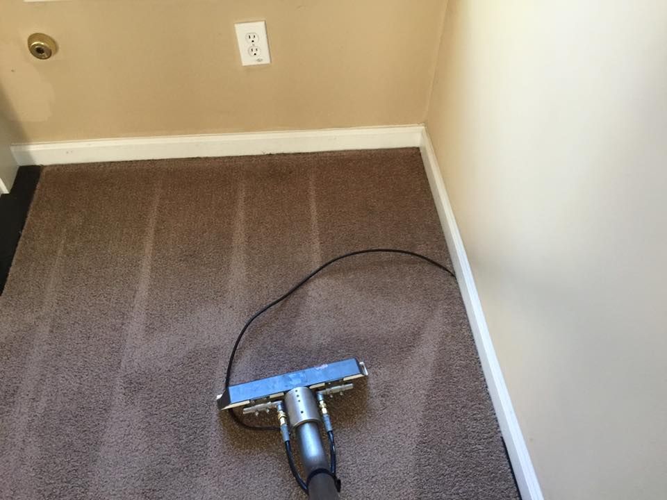 A vacuum cleaner is cleaning a brown carpet in a room.