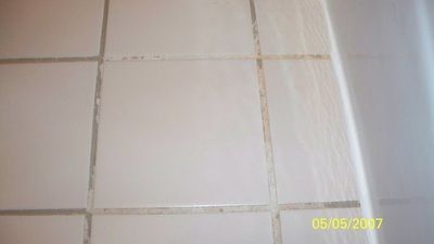 A picture of a tiled floor with a bathtub in the background.