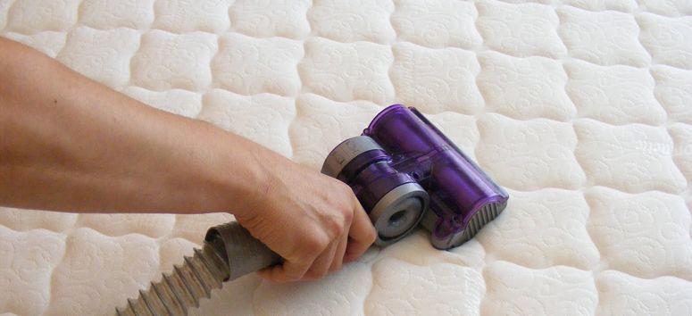 A person is cleaning a mattress with a vacuum cleaner.