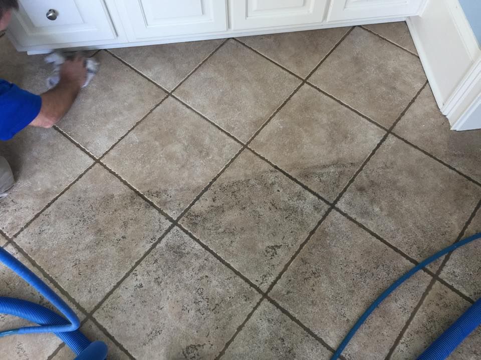 A man is cleaning a tile floor with a vacuum cleaner.