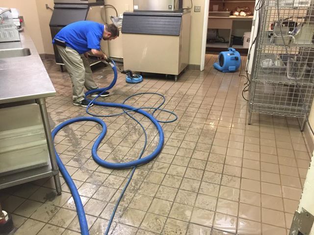 A man is cleaning the floor of a kitchen with a vacuum cleaner.