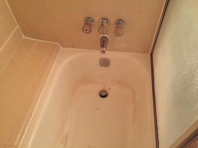 A bathtub with three faucets and a drain in a bathroom.