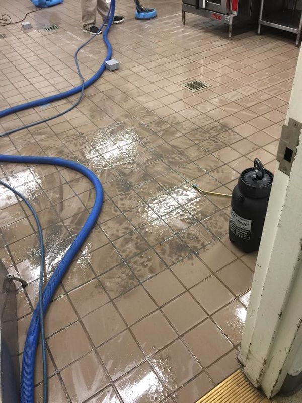 A vacuum cleaner is being used to clean a tiled floor in a kitchen.