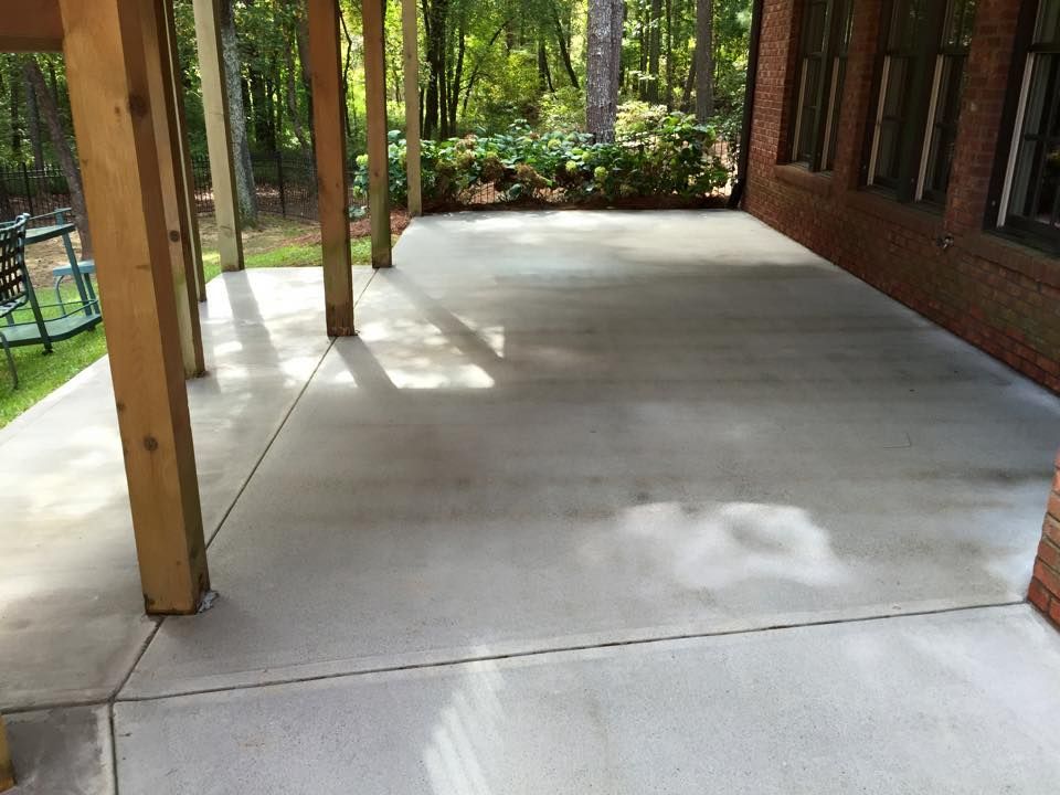 A concrete patio with a wooden roof and trees in the background.