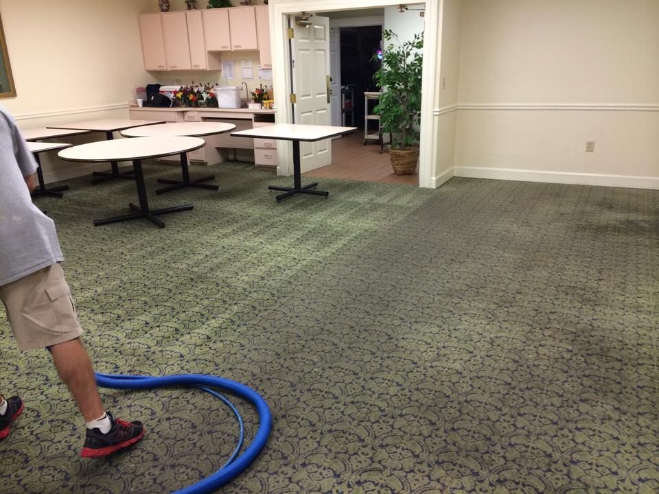 A man is vacuuming the floor of a room with tables