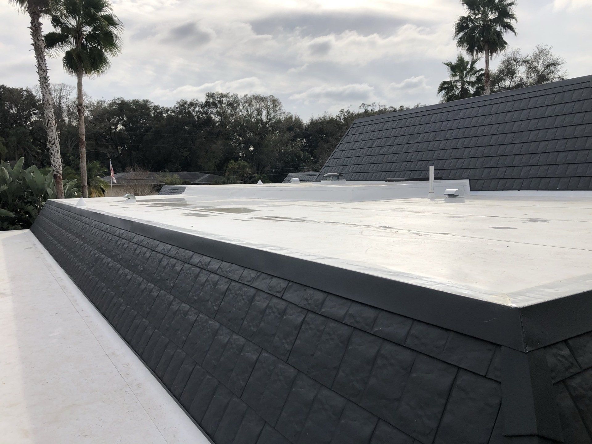 A white roof with black tiles on it and palm trees in the background.