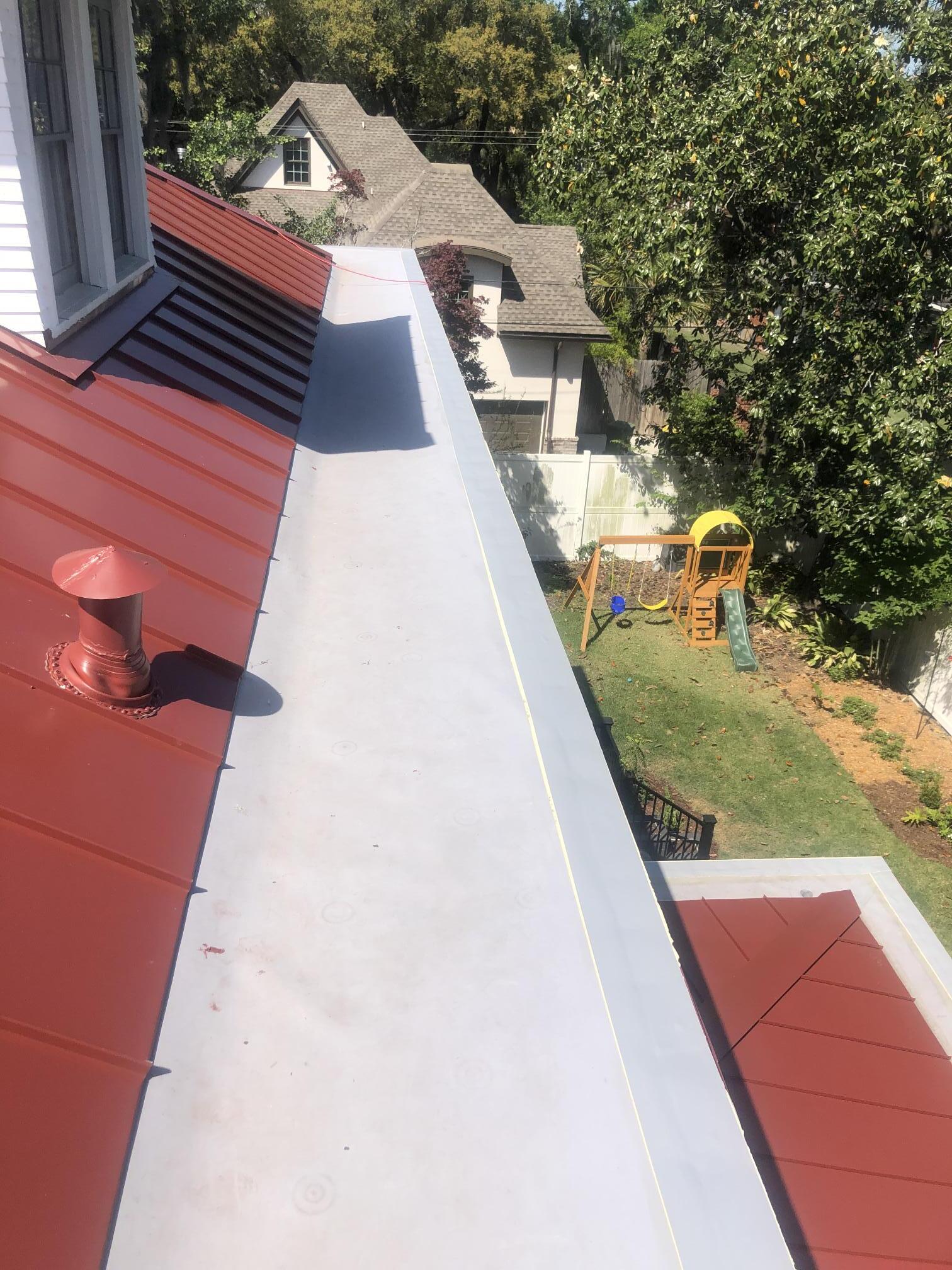 A red roof with a chimney on it and a playground in the background.