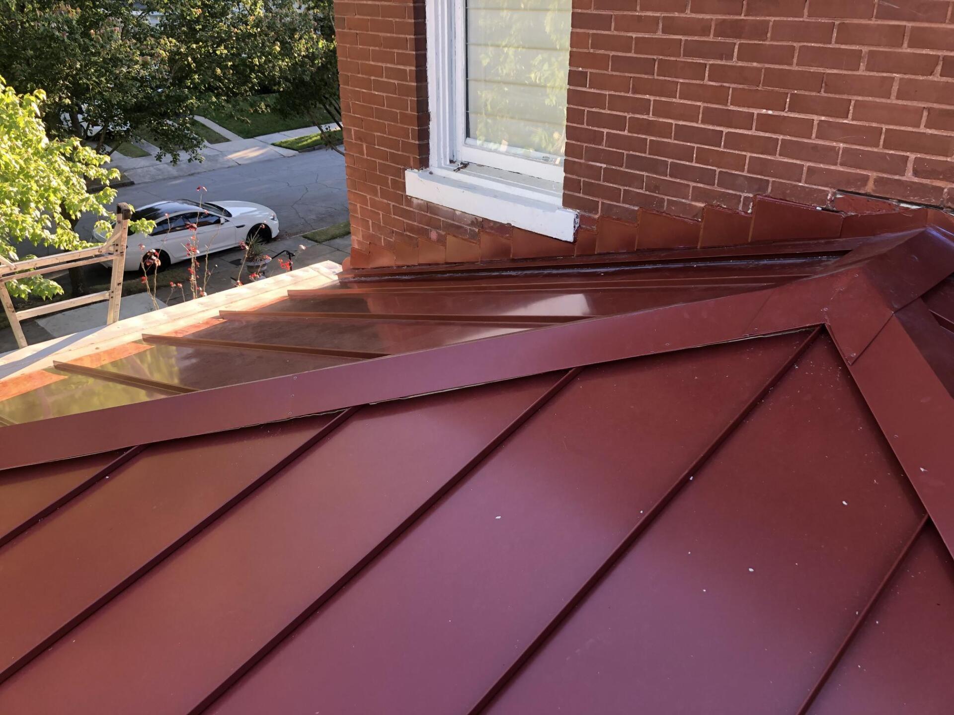 A red roof is sitting on top of a brick building next to a window.