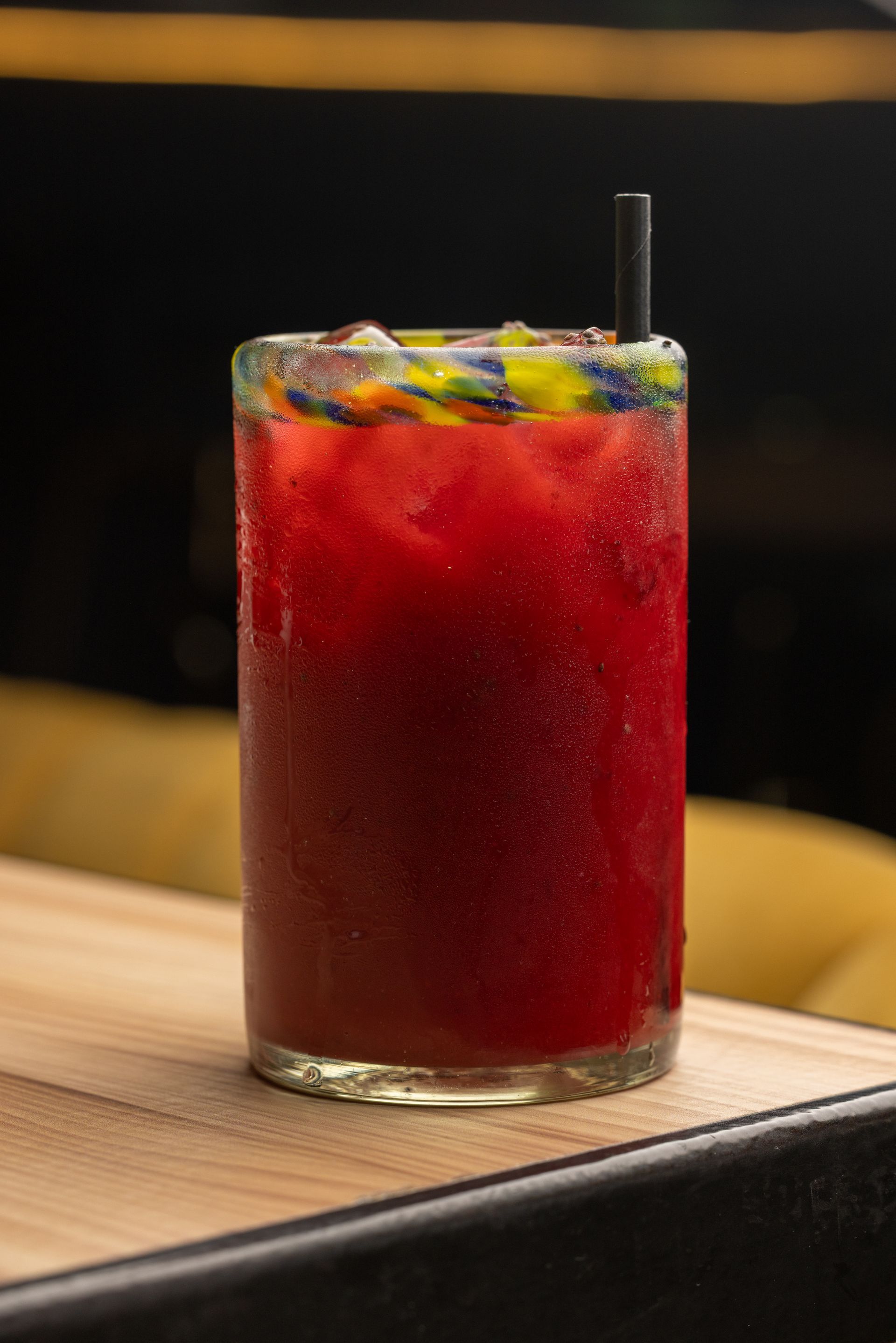 A red drink with a straw in it is sitting on a wooden table.
