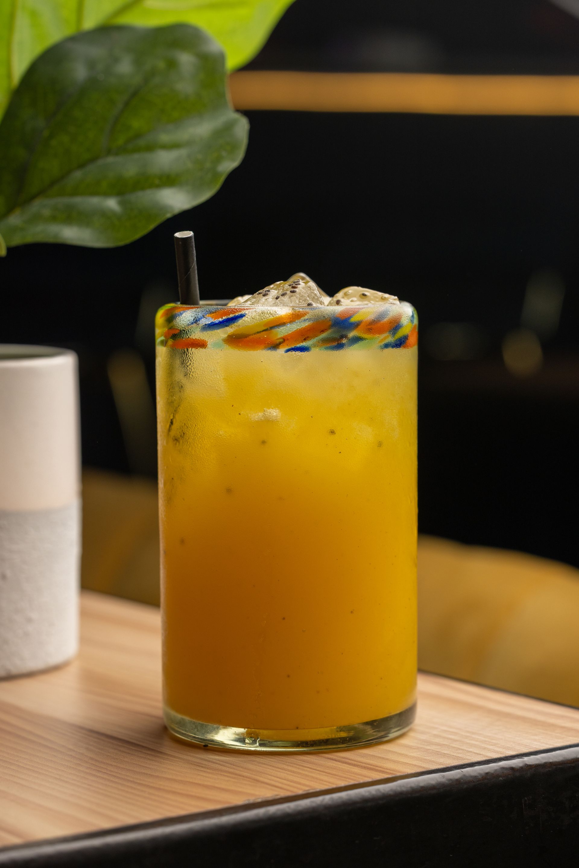 A close up of a glass of orange juice with a straw on a table.