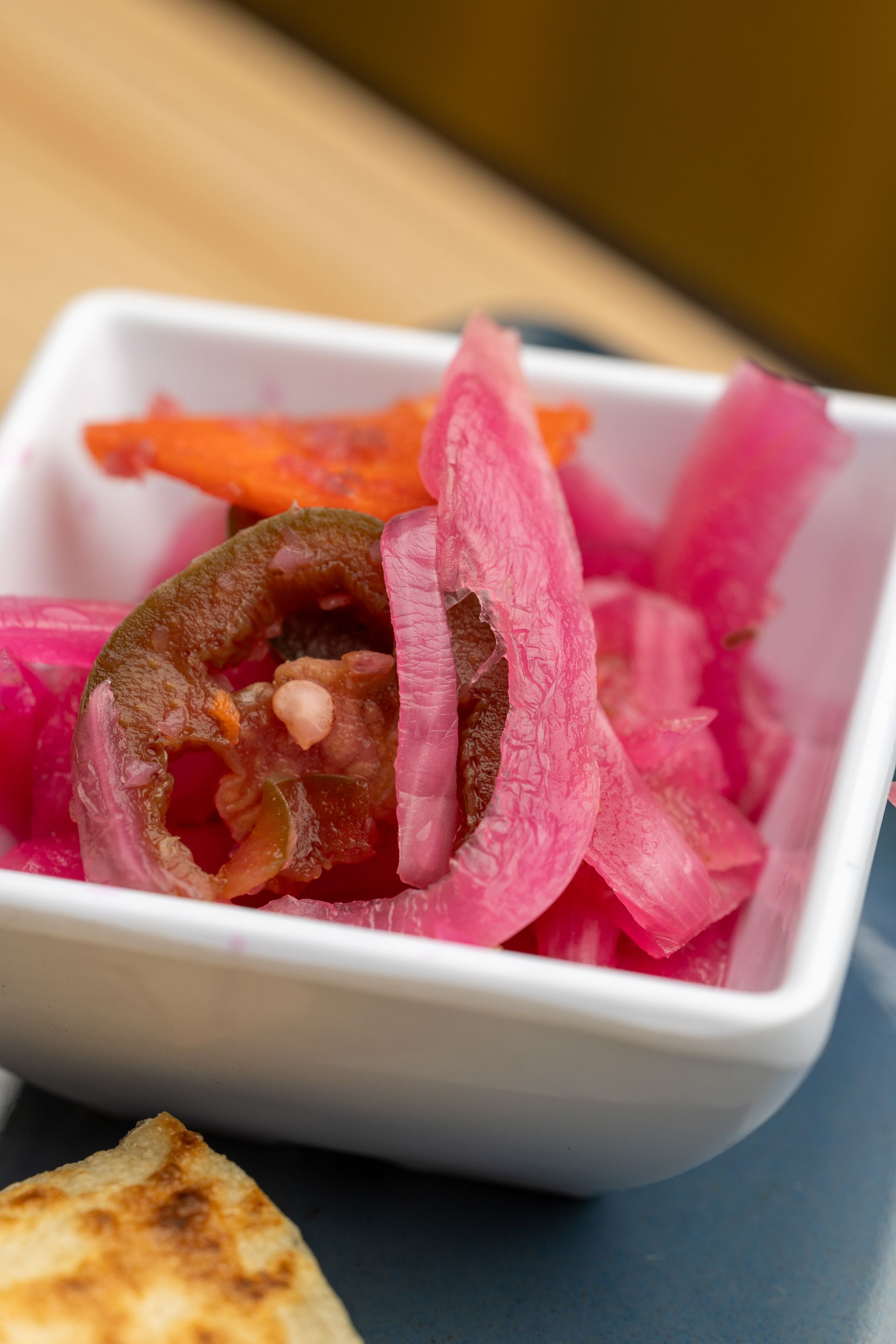 A white bowl filled with pickled onions and carrots on a table.