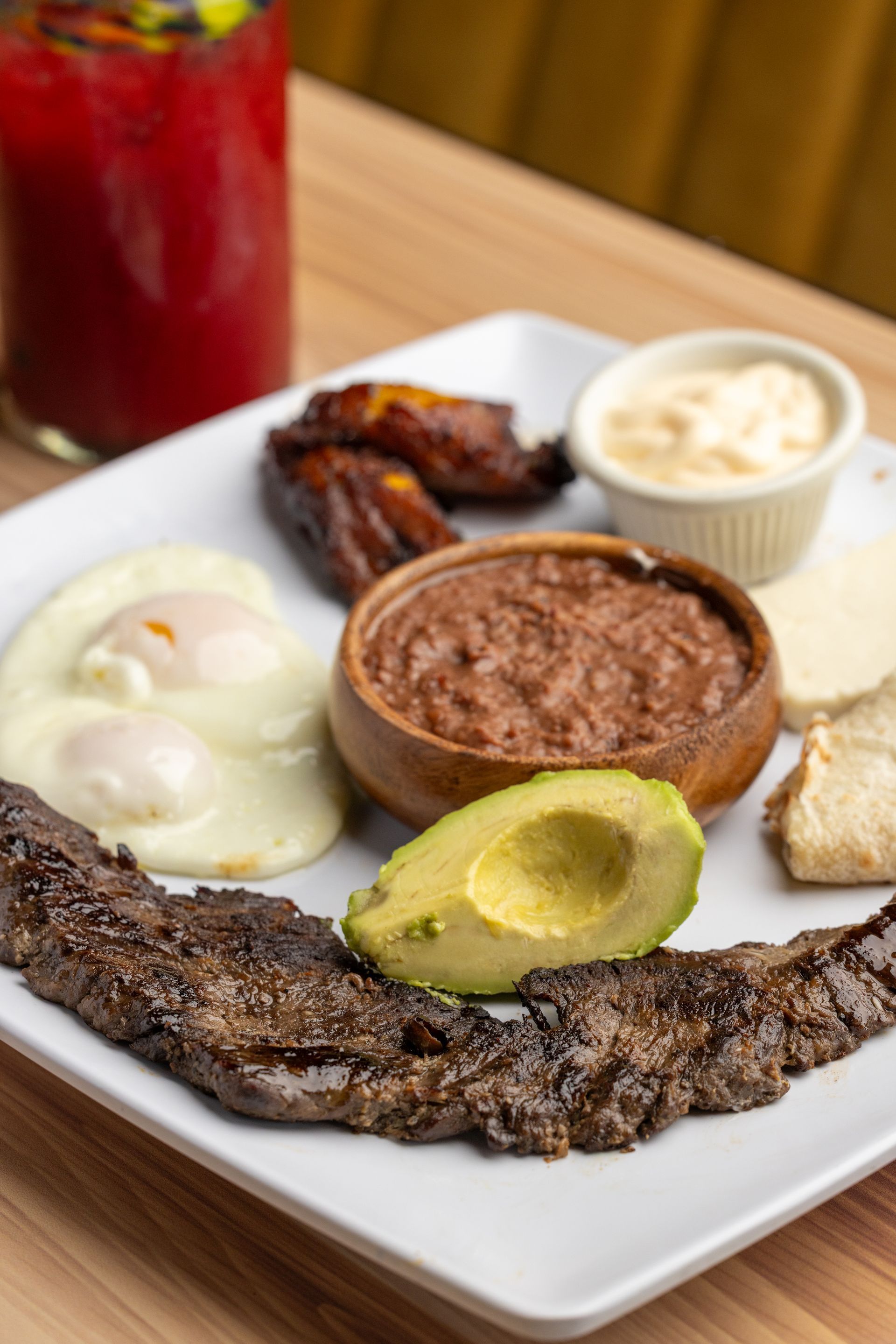 A white plate topped with a steak , eggs , beans , and avocado.