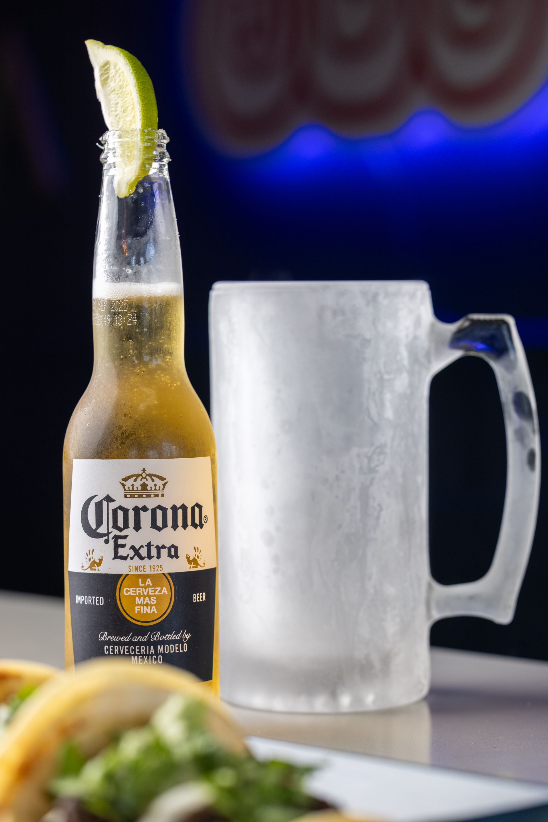 A bottle of corona extra beer next to a glass mug on a table.