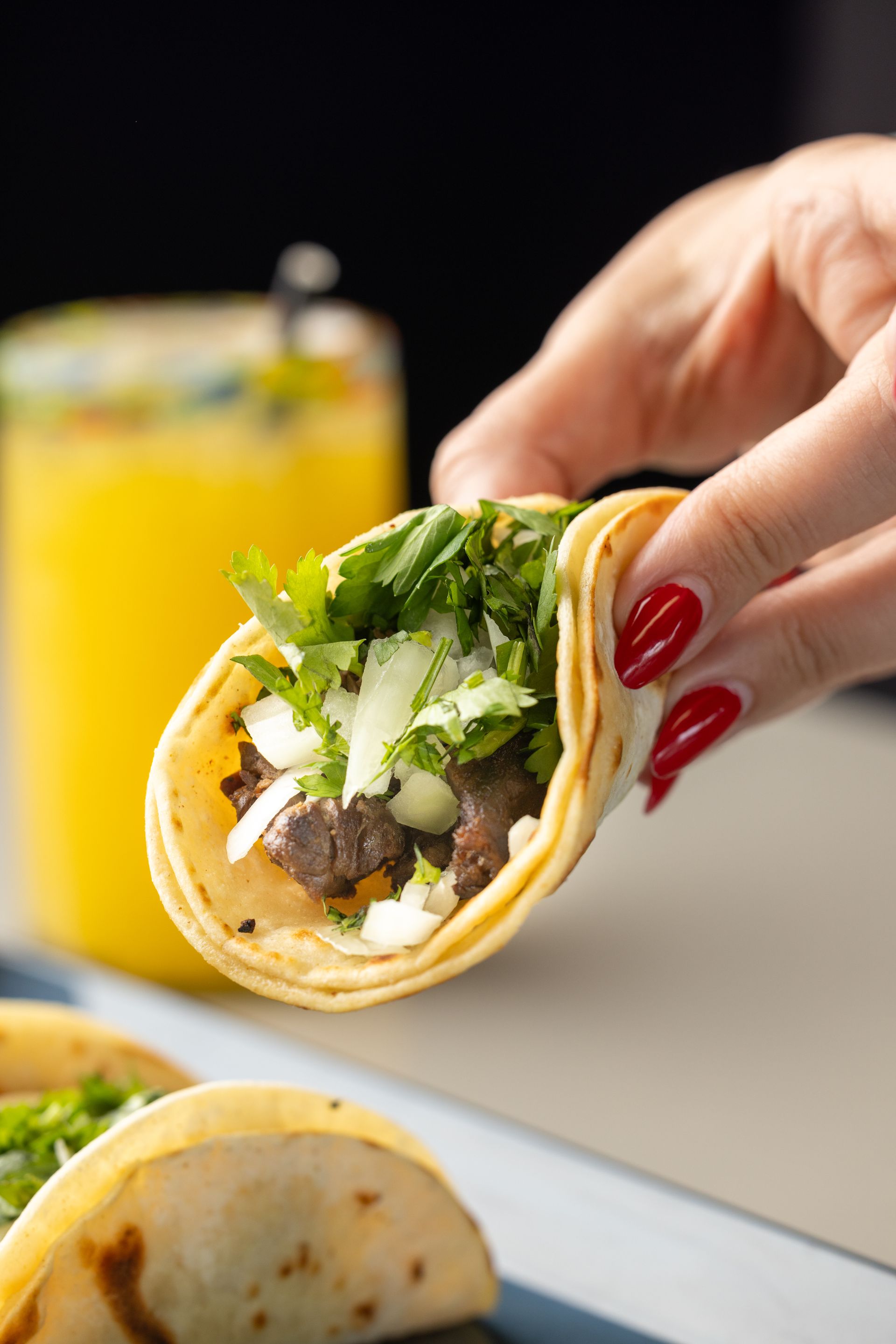 A person is holding a taco with a drink in the background.