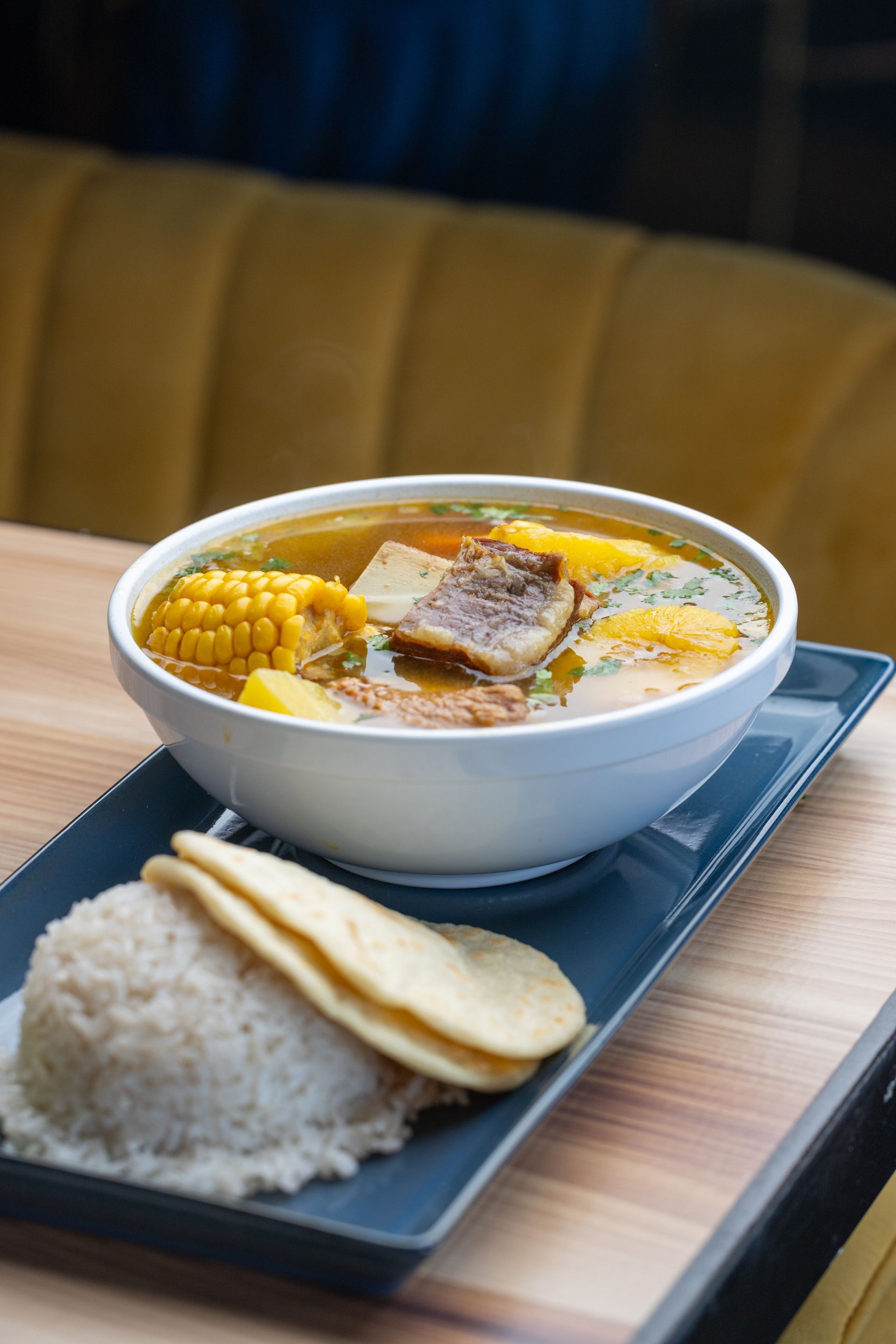 Bowl of soup with corn and potatoes, served with rice and flatbread on a blue plate.