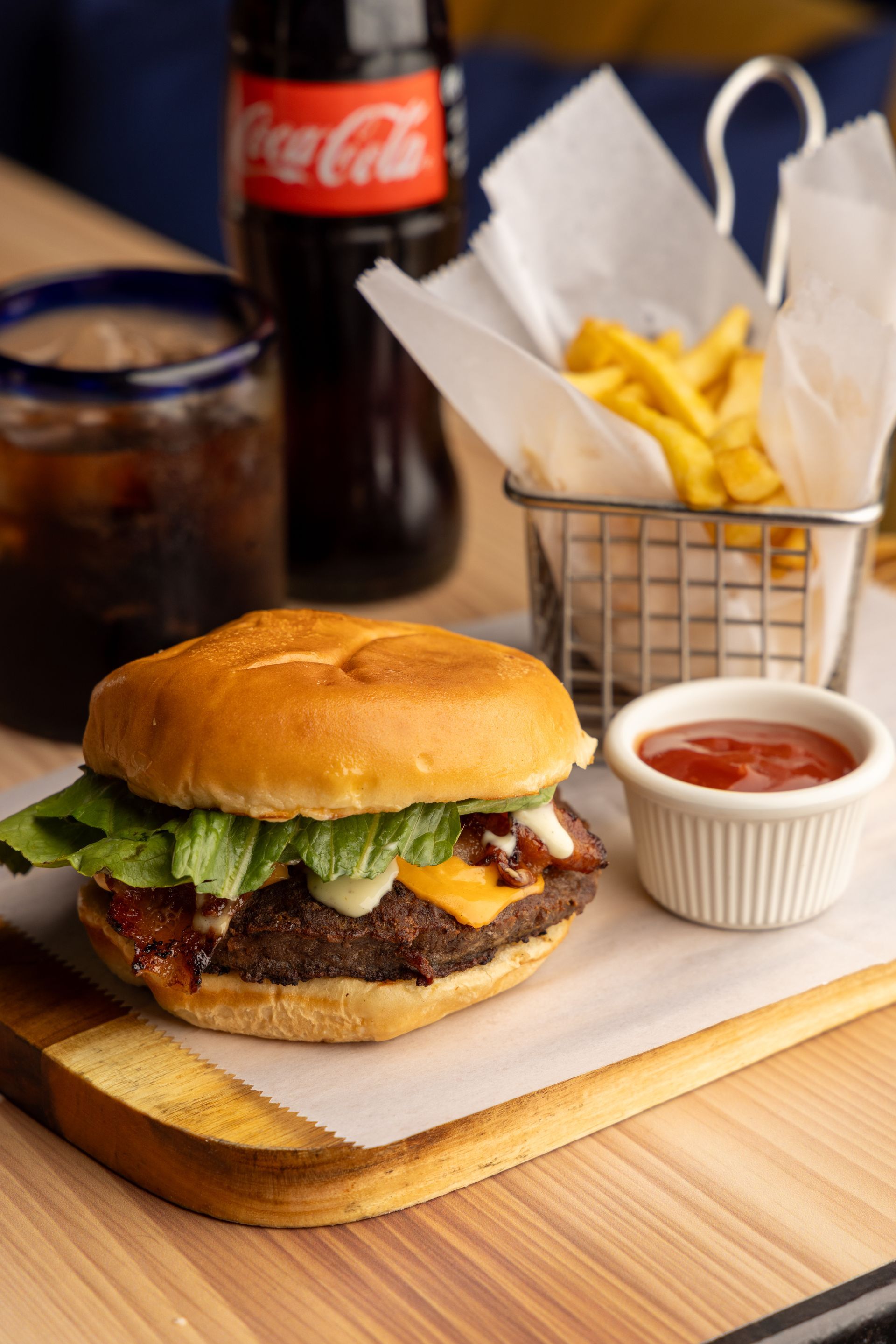 Burger with fries, ketchup, and Coca-Cola on a wooden board.