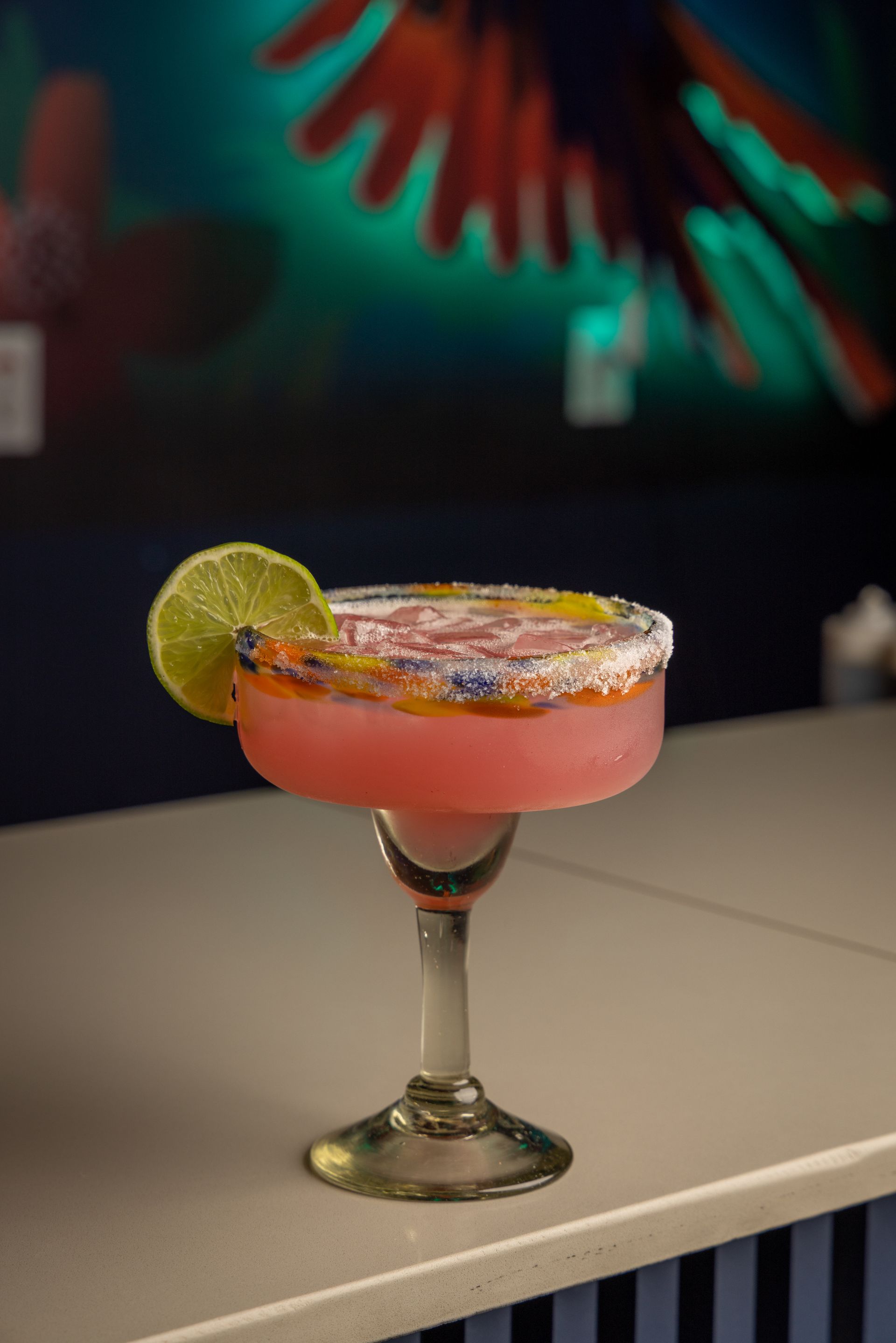 Pink margarita in a stemmed glass with a lime garnish, on a bar.