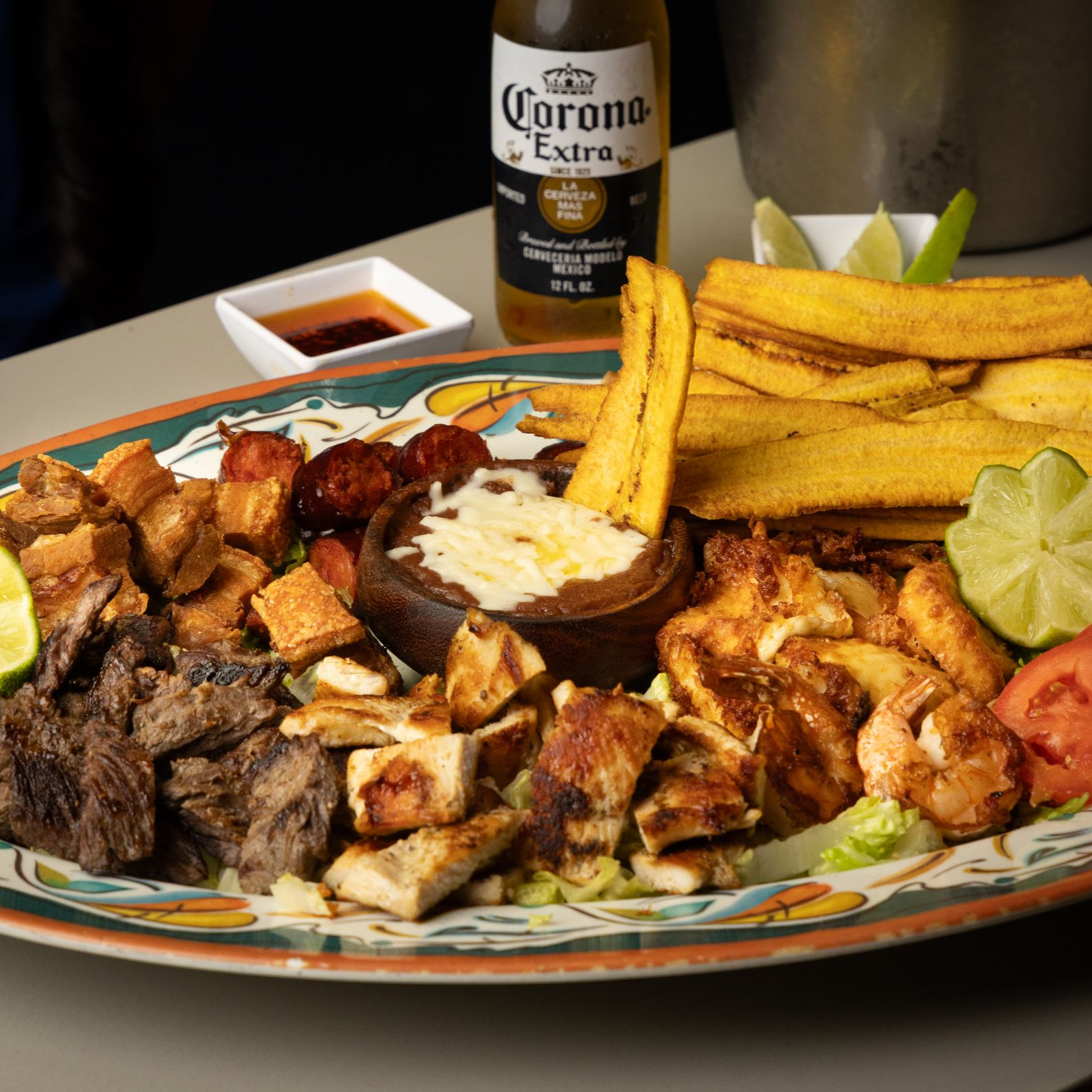 Large platter with grilled meats, fried plantains, cheese dip, Corona beer, lime slices.