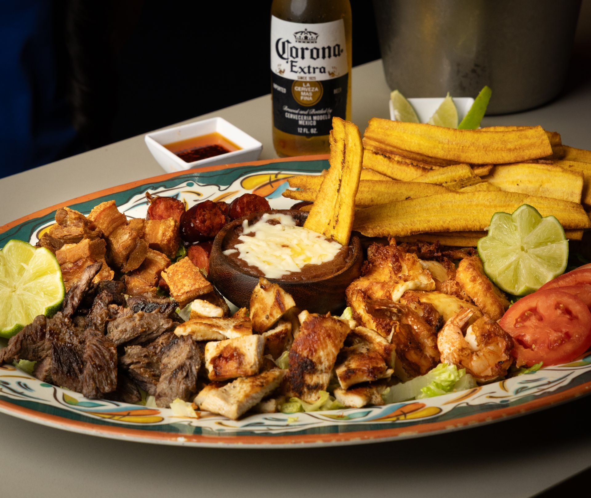 Platter of grilled meats, plantains, and dip with a Corona beer and limes.