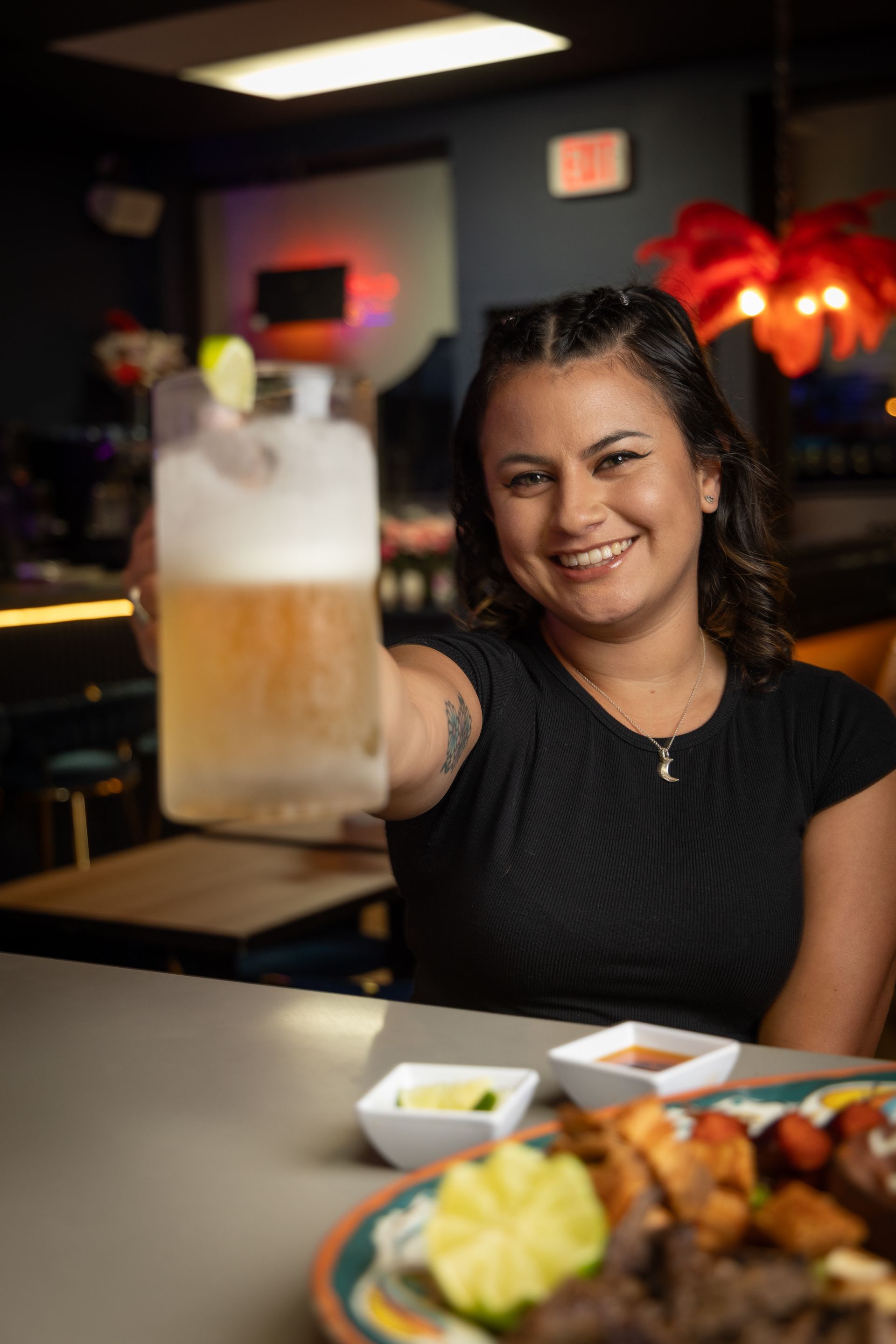 Woman holding beer in a frosted glass, smiling at the camera in a restaurant.