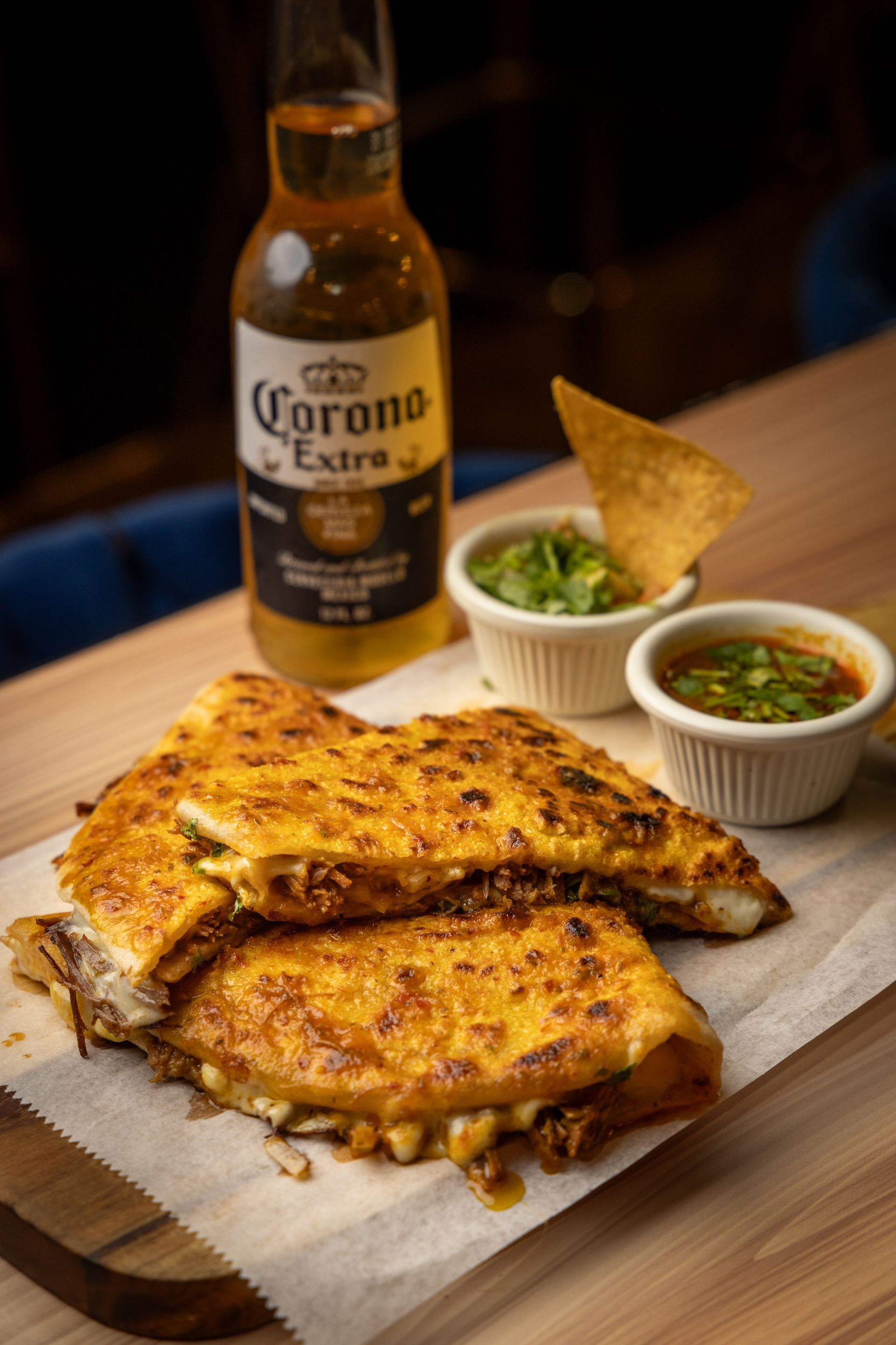 Quesadilla with guacamole and salsa, beer bottle on wooden board.