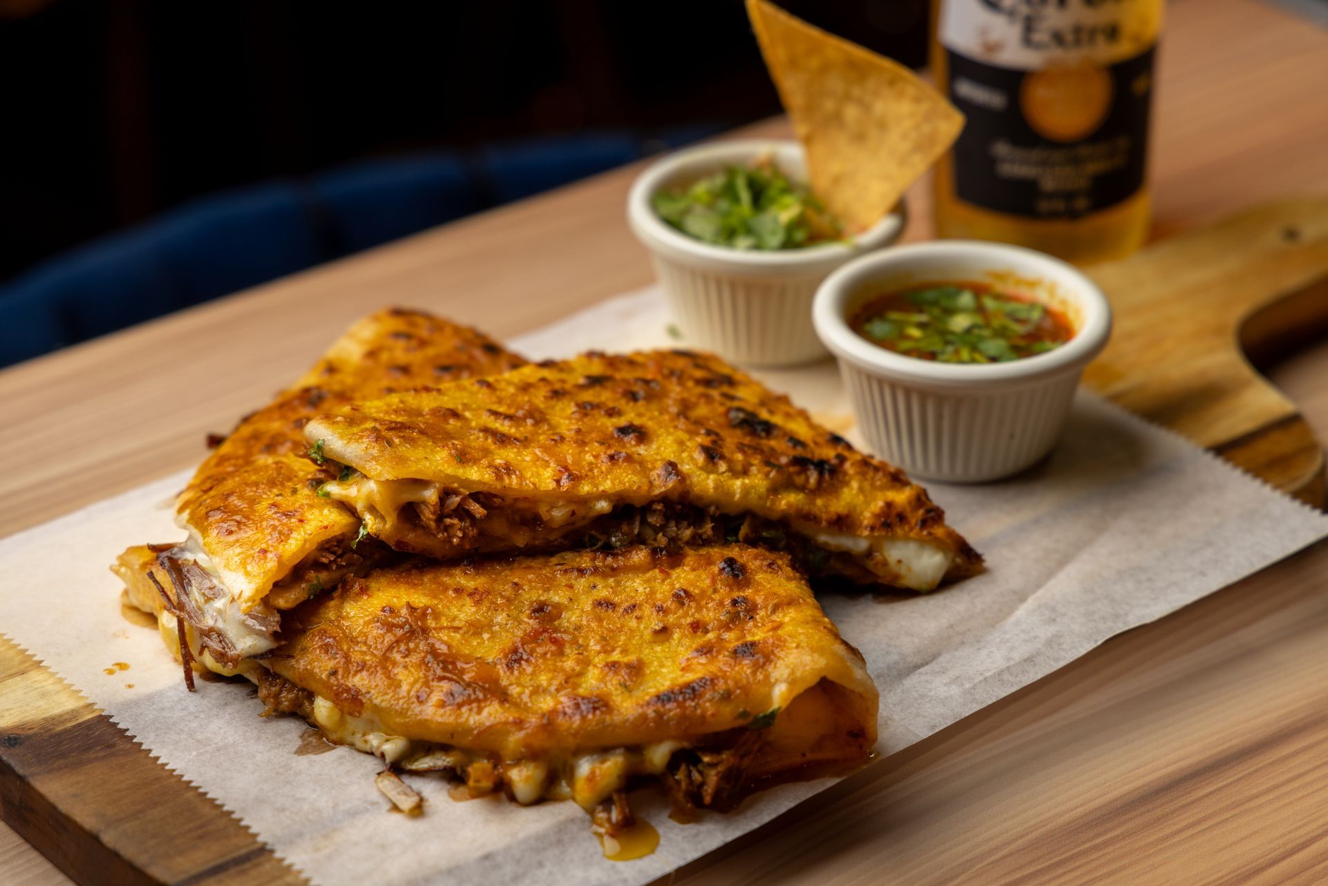Quesadilla with guacamole and salsa, served on a wooden board with a beer.