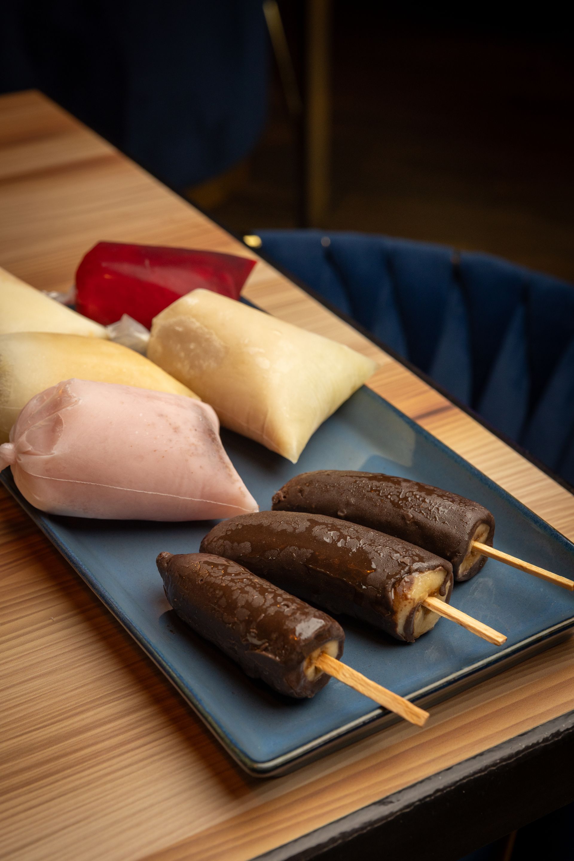 Plate of colorful frozen treats: ice pops and chocolate-covered bananas on a wooden table.
