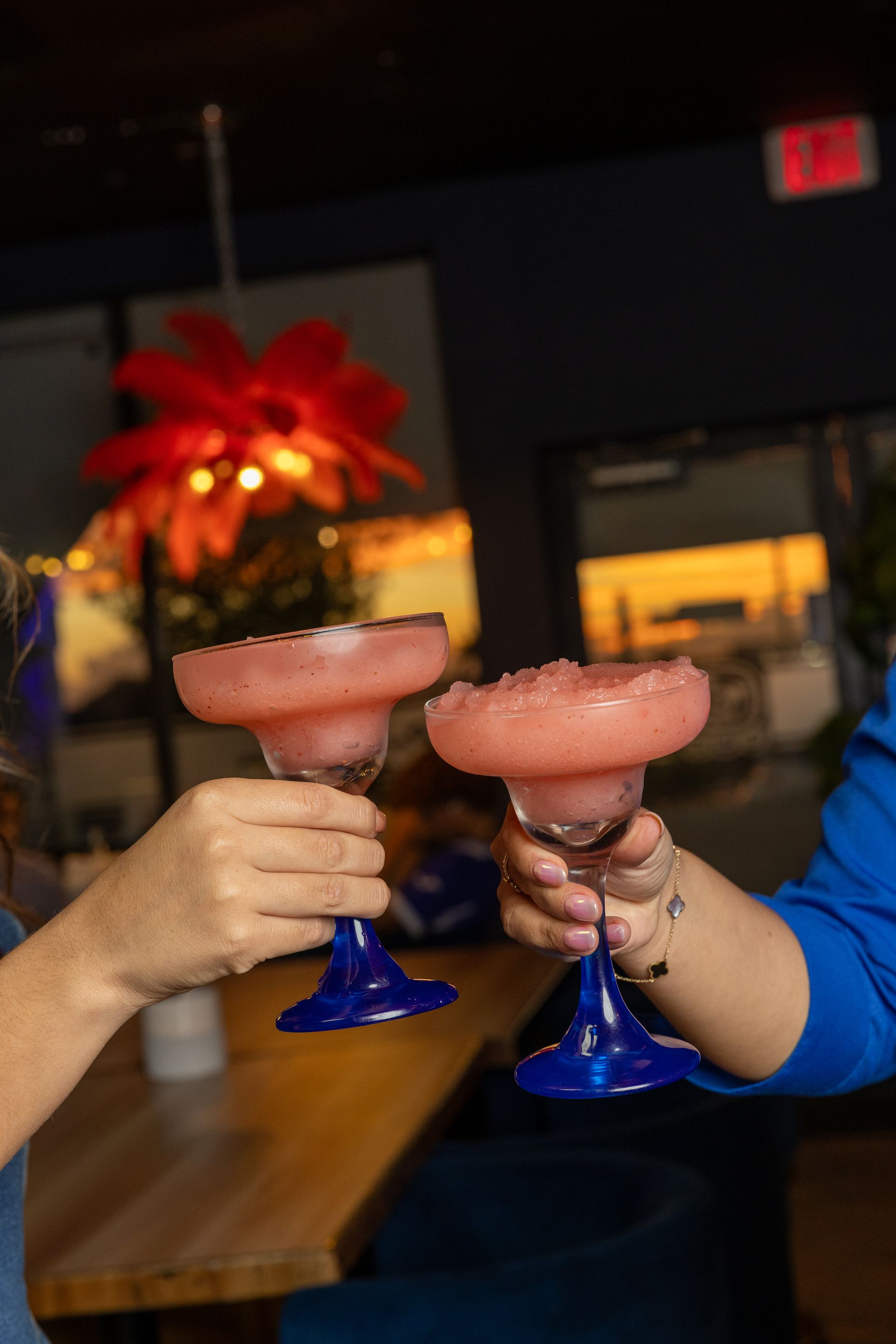Two people toasting with pink margaritas in blue-stemmed glasses.