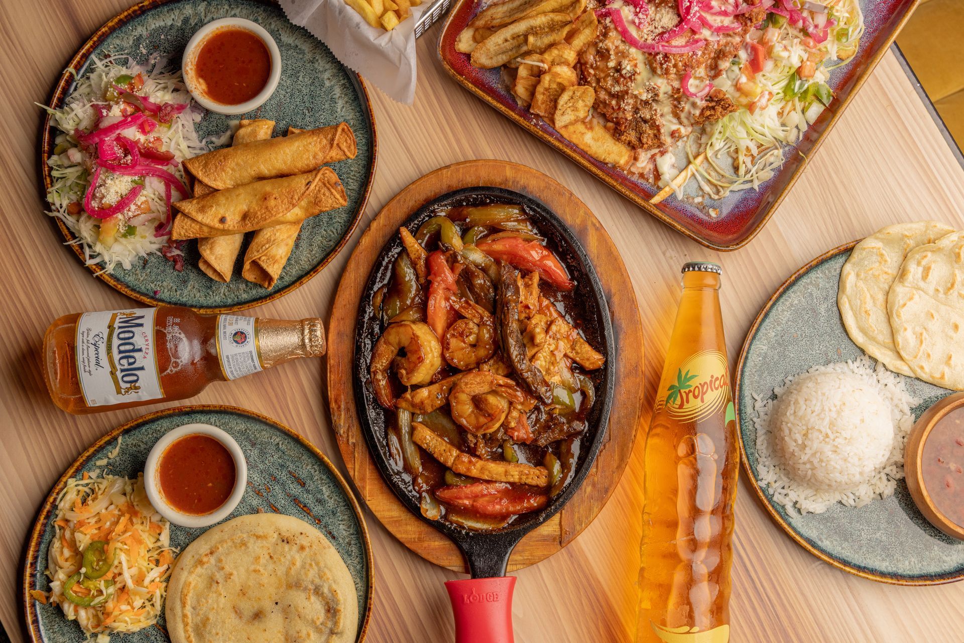 Assorted Mexican dishes on a table, including fajitas, tacos, taquitos, rice, beans, and beer.