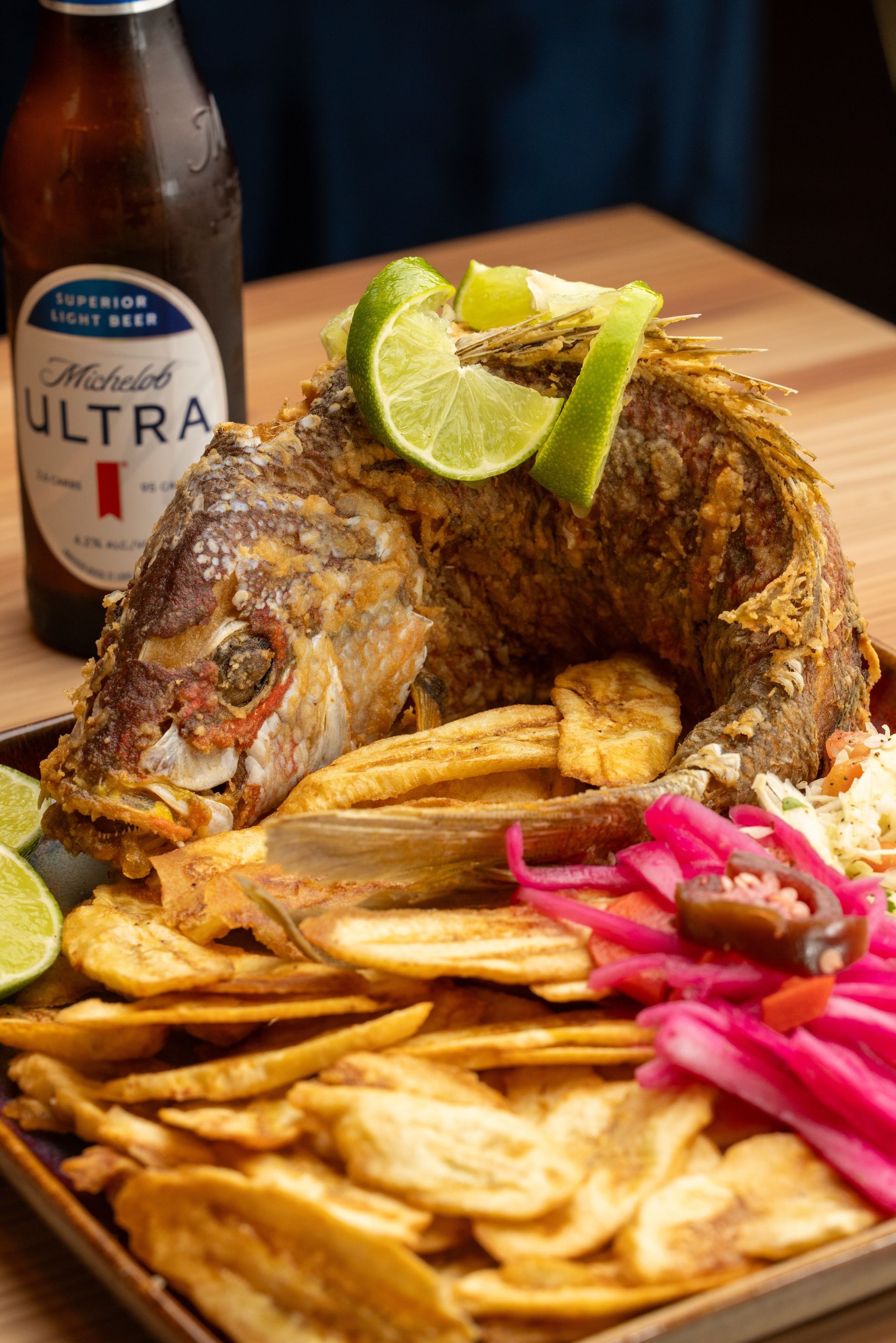 Fried whole fish with plantain chips, pickled onions, and lime, served with a beer.