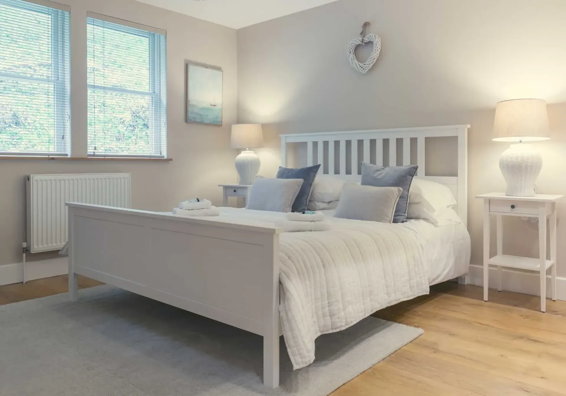 Cozy bedroom with white bed frame, nightstands, lamps, and blue accents.