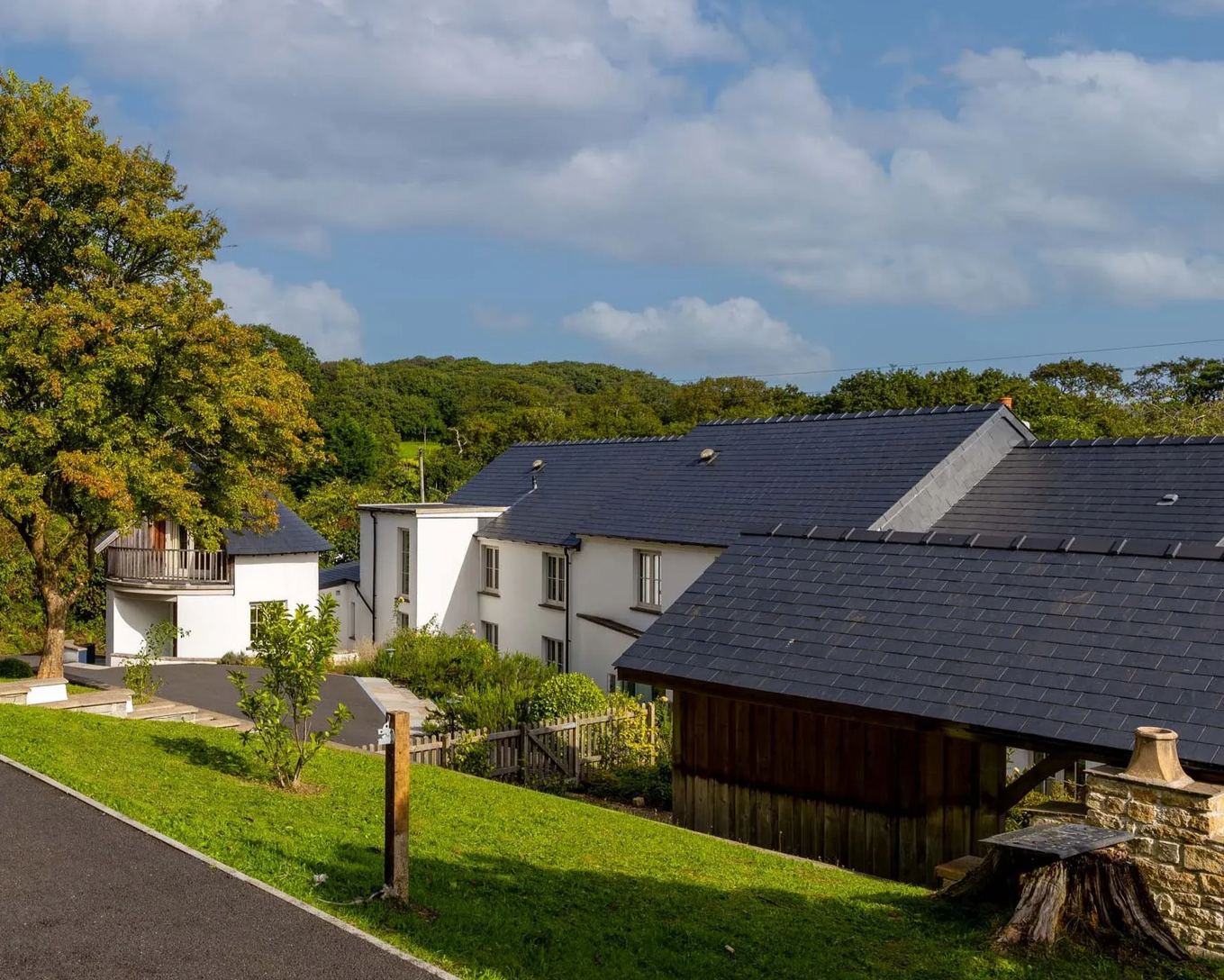 Buildings with dark gray roofs, surrounded by trees and a green lawn, under a cloudy sky.