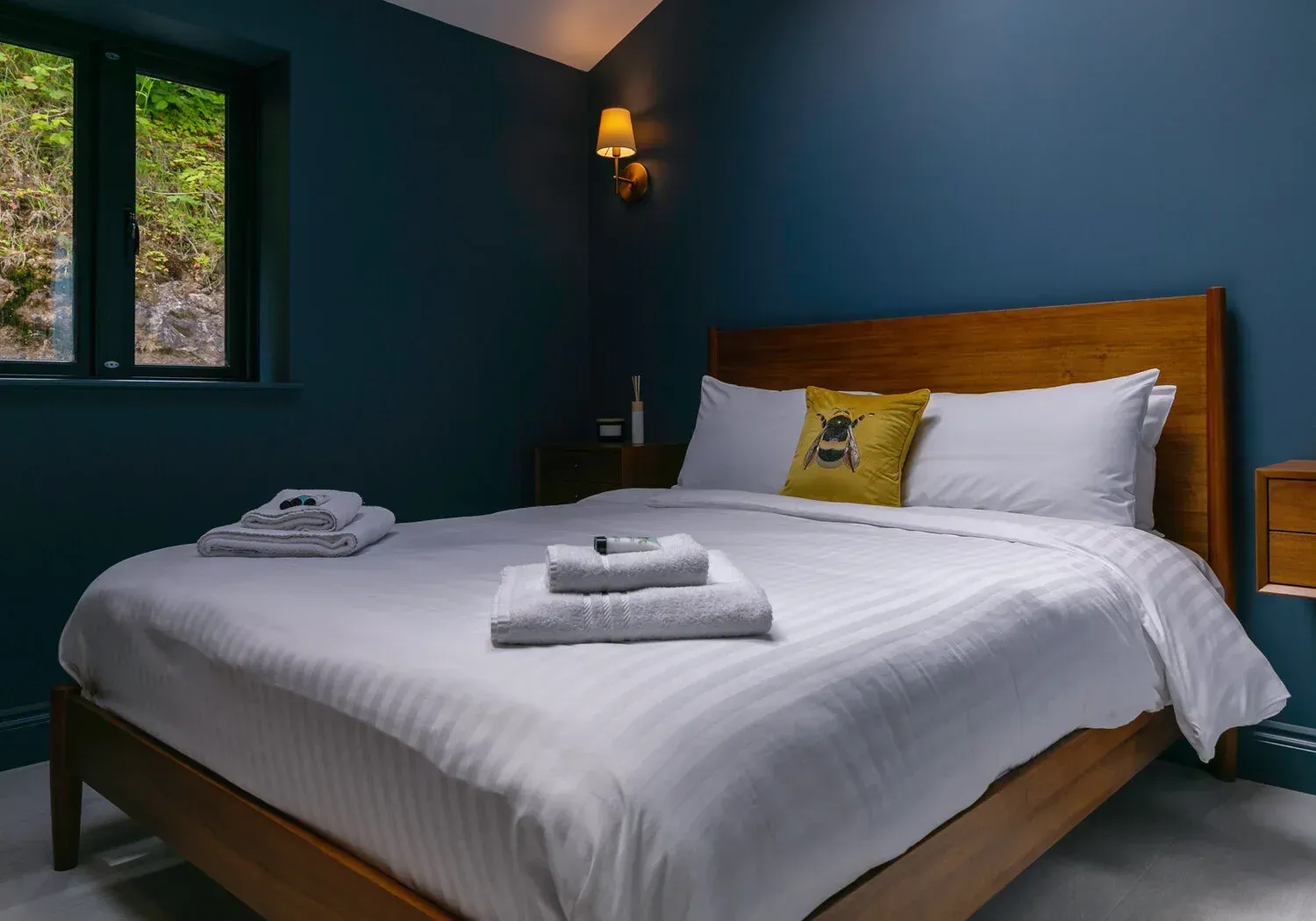 Bedroom with a wooden bed, white linens, and blue walls. A window is on the left.