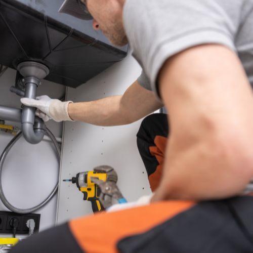 A man is fixing a sink with a drill