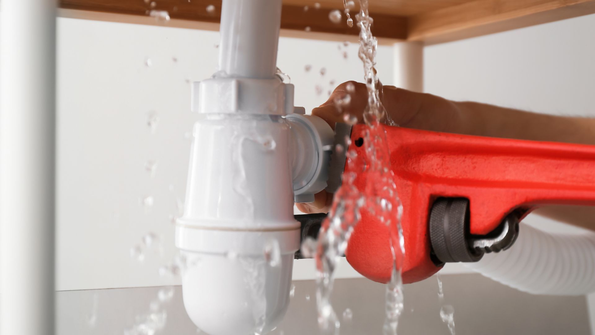 A person is fixing a leaking sink pipe with a wrench.