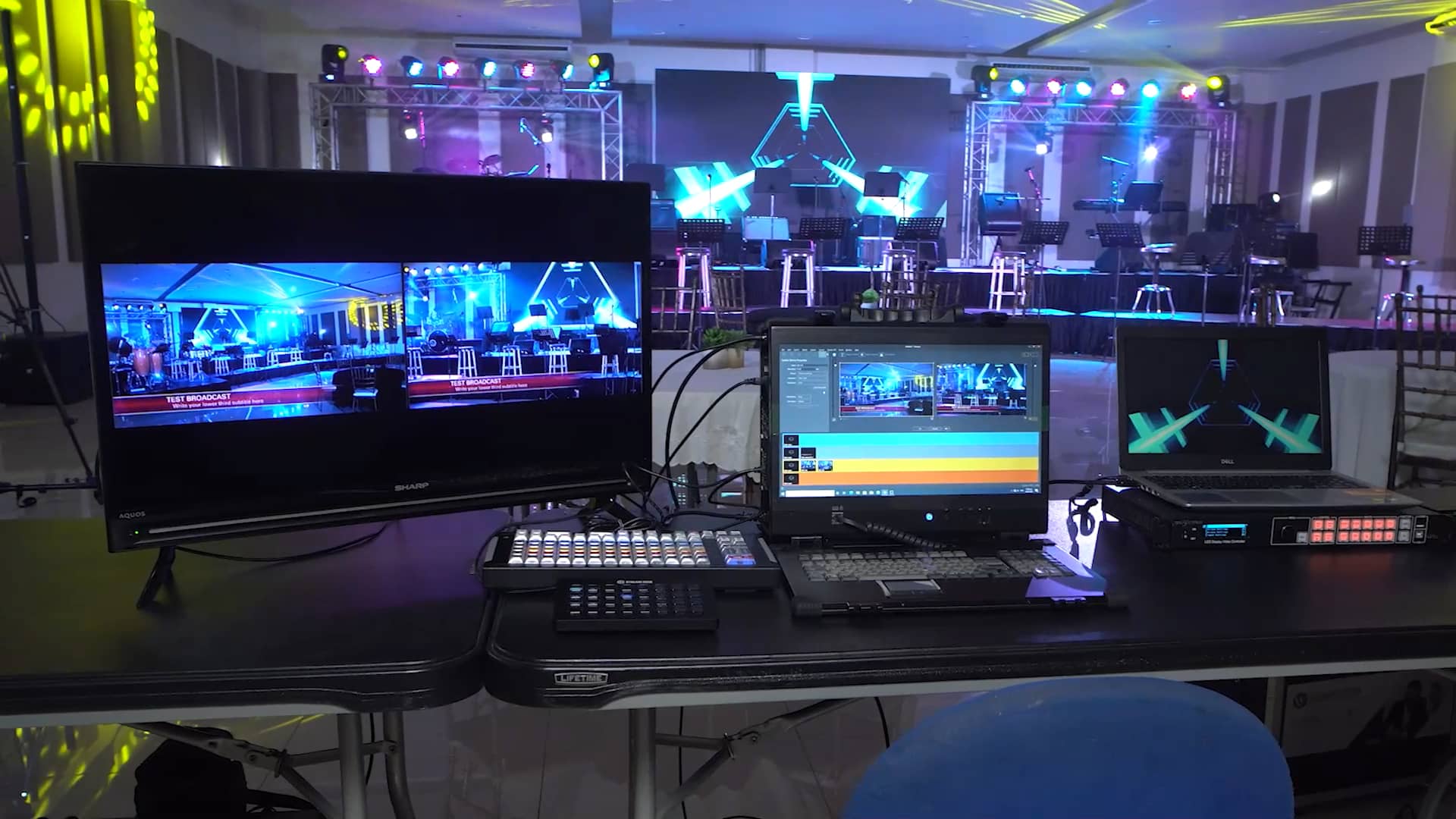 A desk with two monitors and a laptop on it in front of a stage.