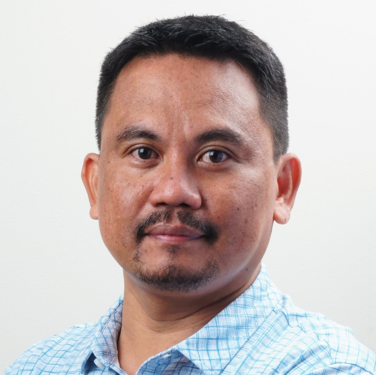 A man with a beard is wearing a blue plaid shirt.