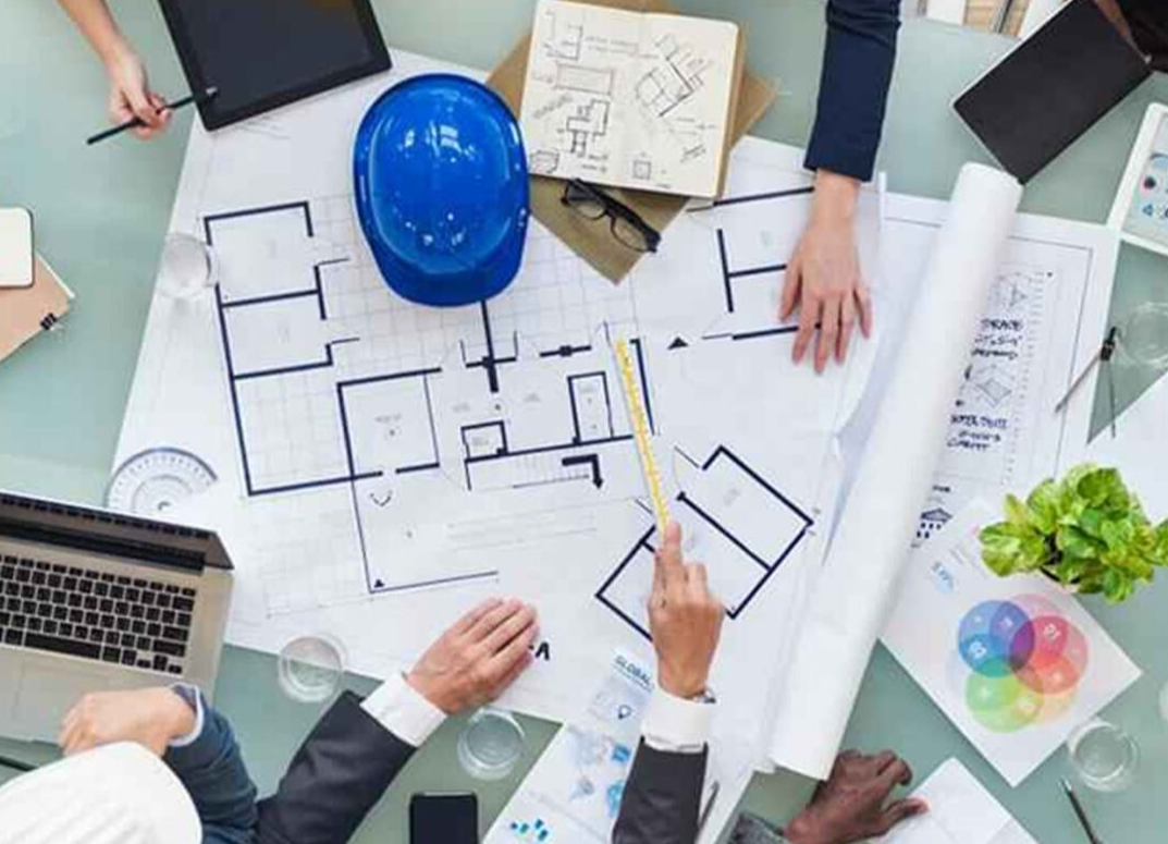 A group of people are sitting around a table looking at a blueprint.
