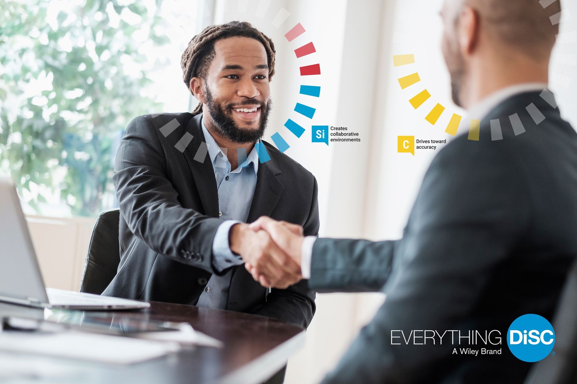 A man in a suit is shaking hands with another man in front of a laptop.